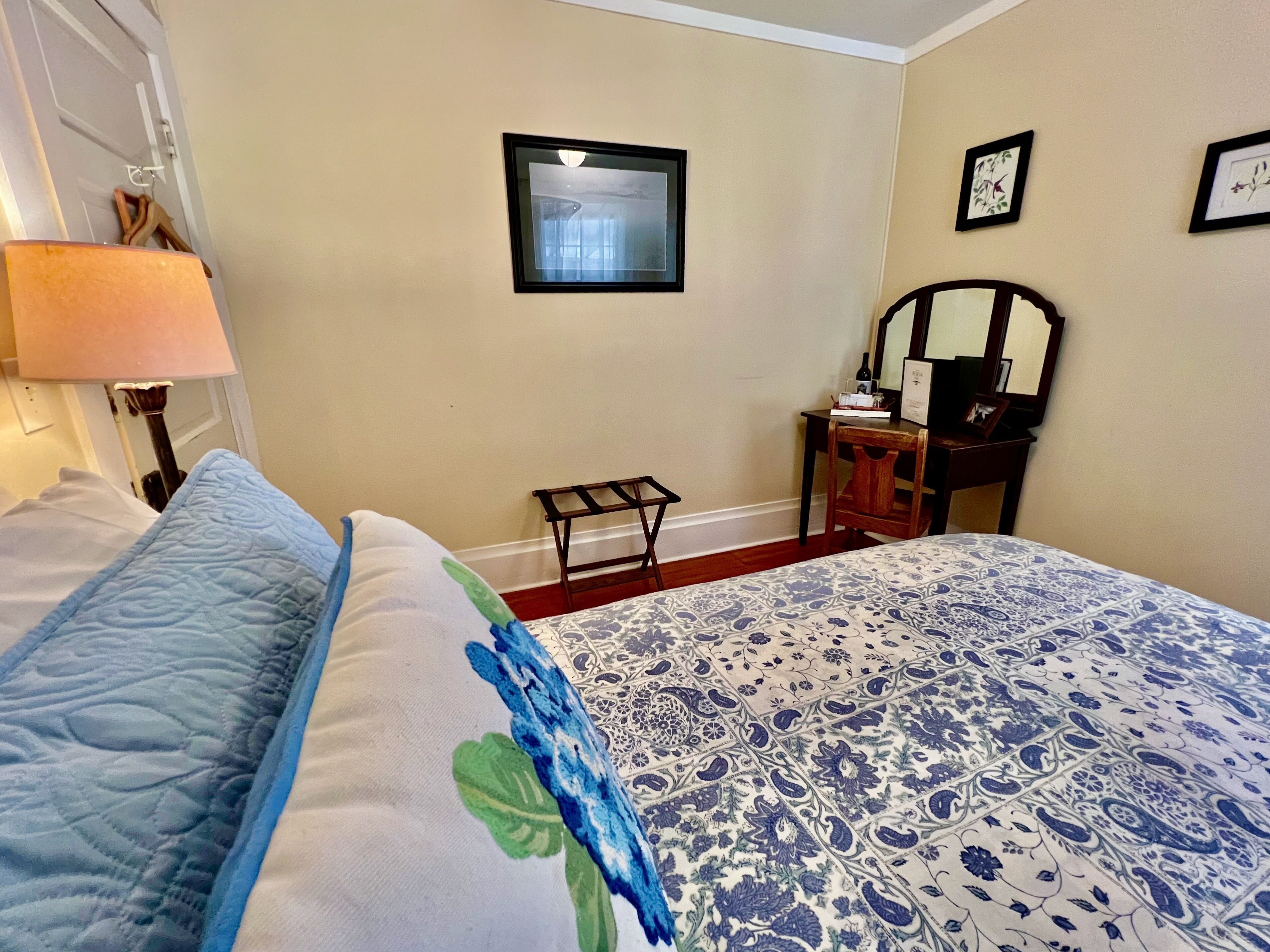A hotel room with a bed, a desk, a chair, a lamp, and a mirror.