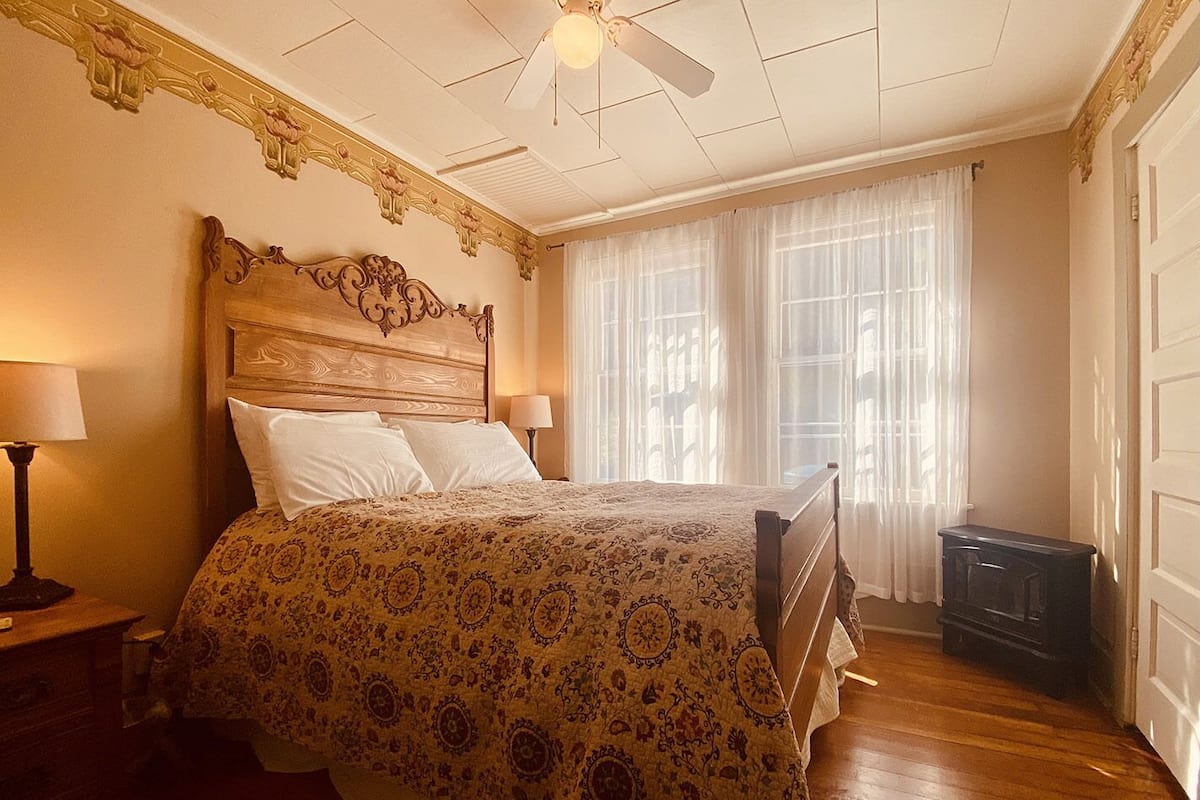 A bedroom with a wooden headboard, a large bed with a patterned bedspread, two bedside lamps, and a ceiling fan.