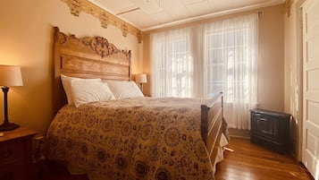 A bedroom with a wooden headboard, a large bed with a patterned bedspread, two bedside lamps, and a ceiling fan.