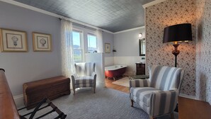 A room with a wooden bench, a striped armchair, a red clawfoot bathtub, and a wall-mounted lamp. - The Historic Requa Inn  (Klamath)