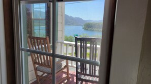 A wooden chair on a balcony with a view of a lake and mountains.