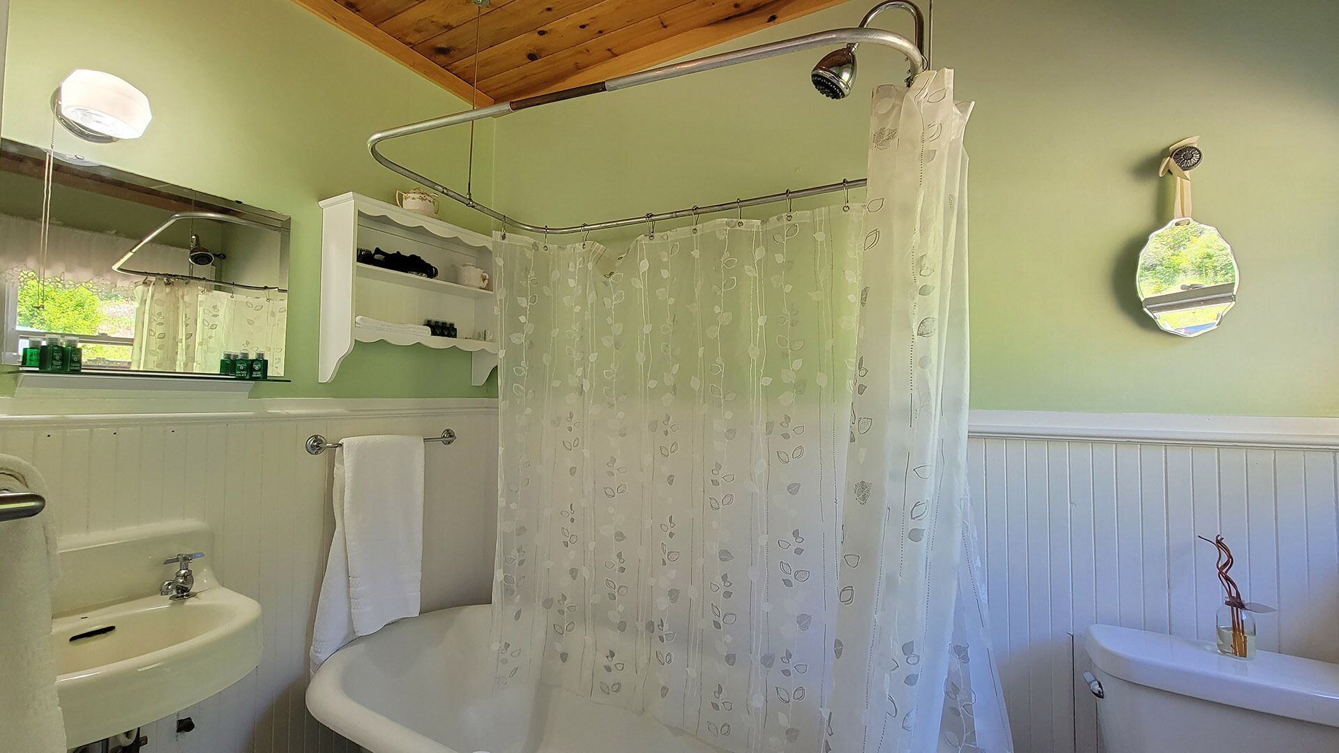 A bathroom with a bathtub, a shower curtain, a sink, a mirror, and a shelf with toiletries.