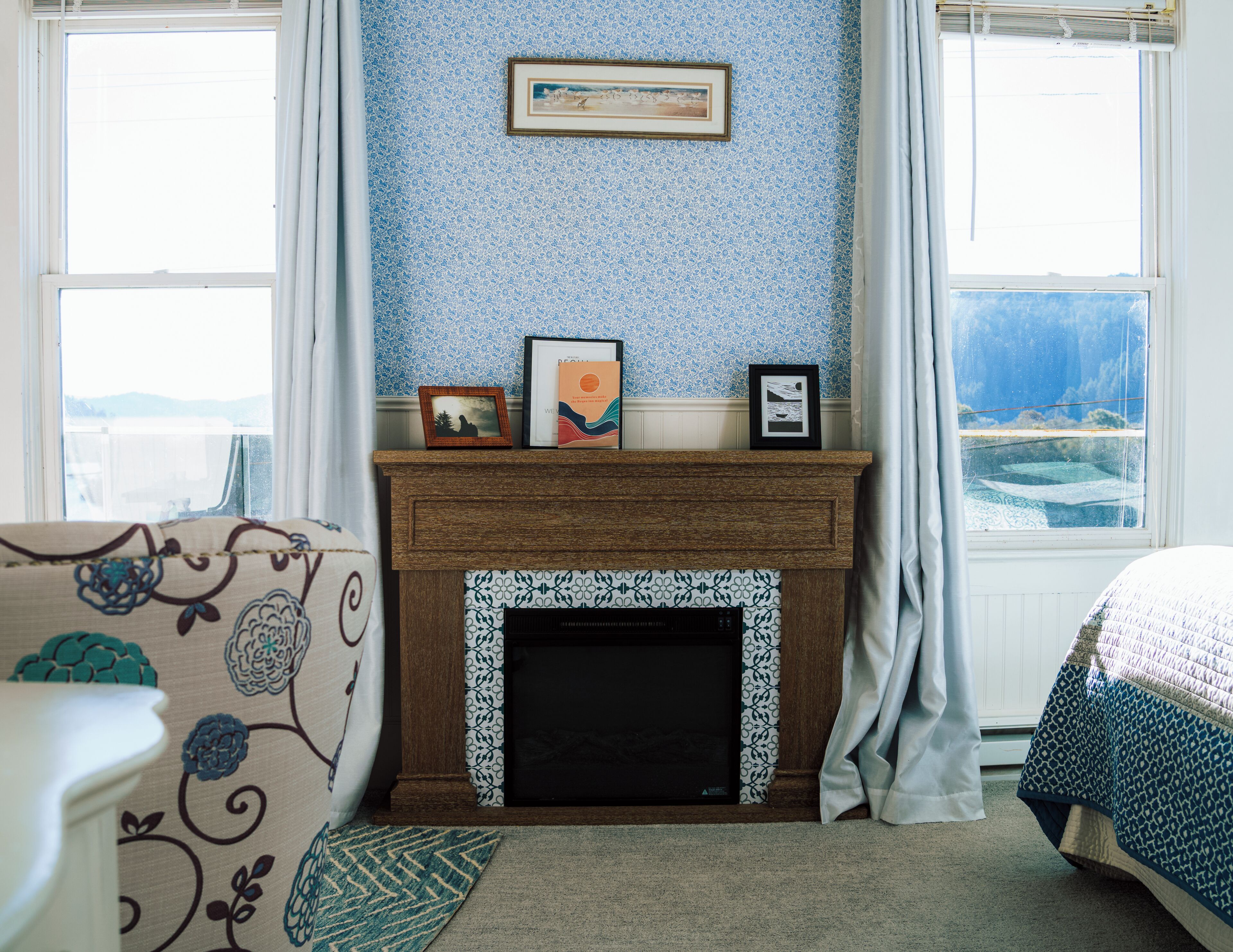 Un dormitorio con chimenea, una cama, un ventanal con vistas y un papel tapiz azul con estampado.