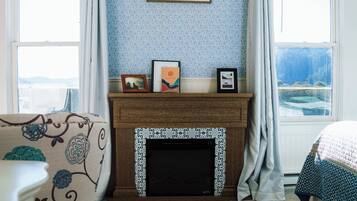 Un dormitorio con chimenea, una cama, un ventanal con vistas y un papel tapiz azul con estampado.