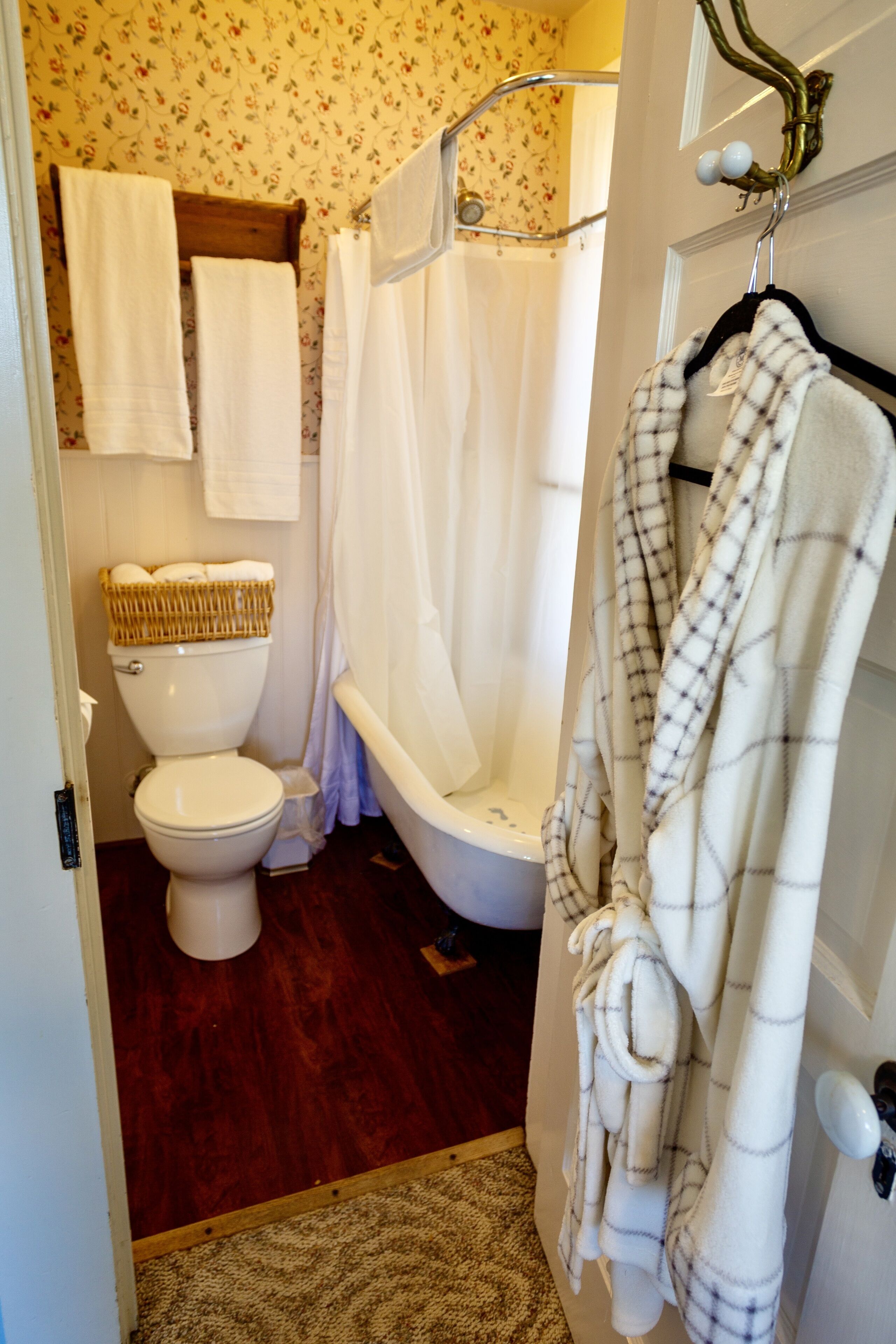 Een badkamer met een toilet, een badkuip en een douchegordijn. Handdoeken hangen aan de muur en er ligt een badjas aan een haak.