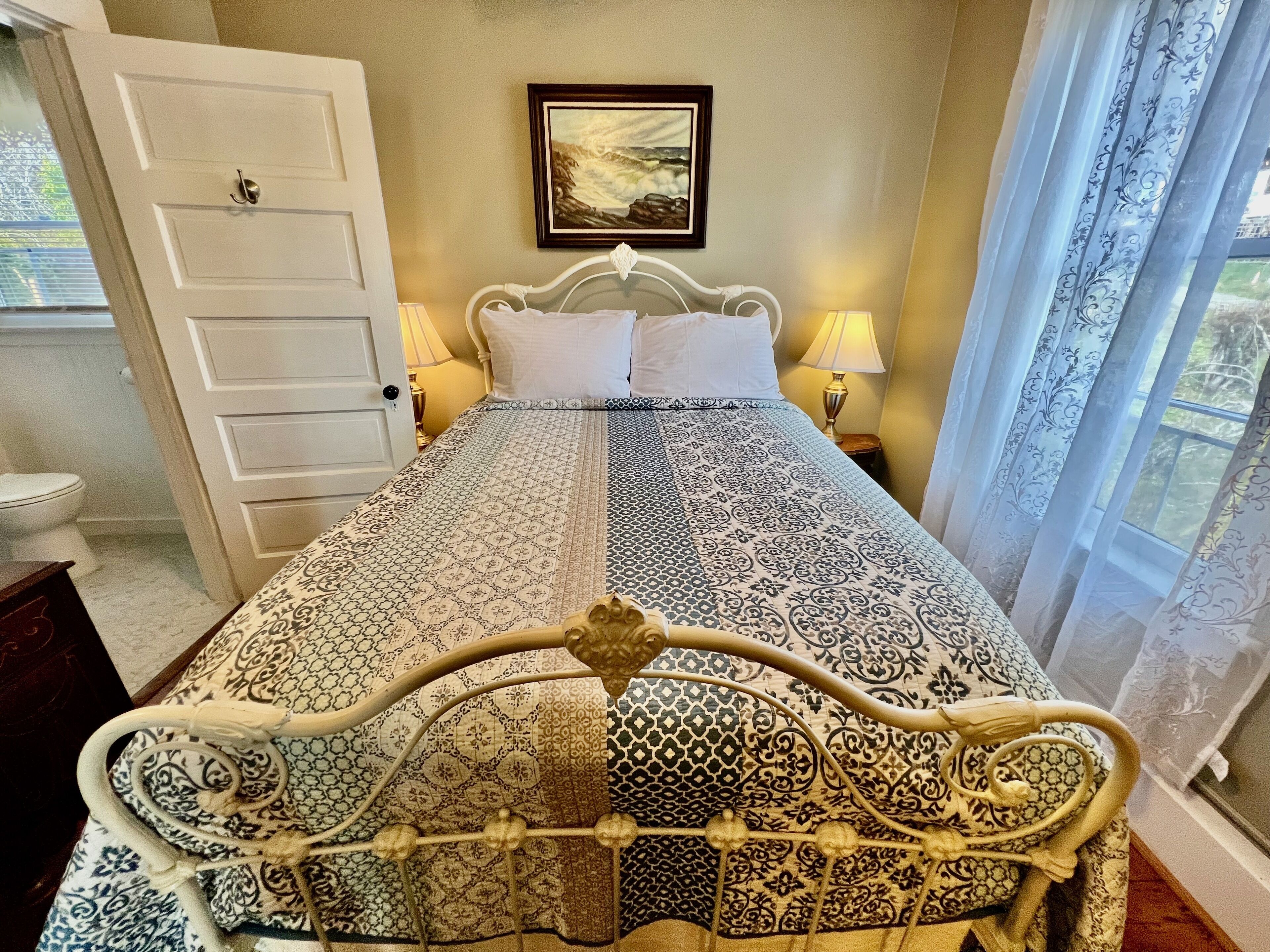 A neatly made bed with a patterned bedspread, two bedside lamps, and a framed picture on the wall.