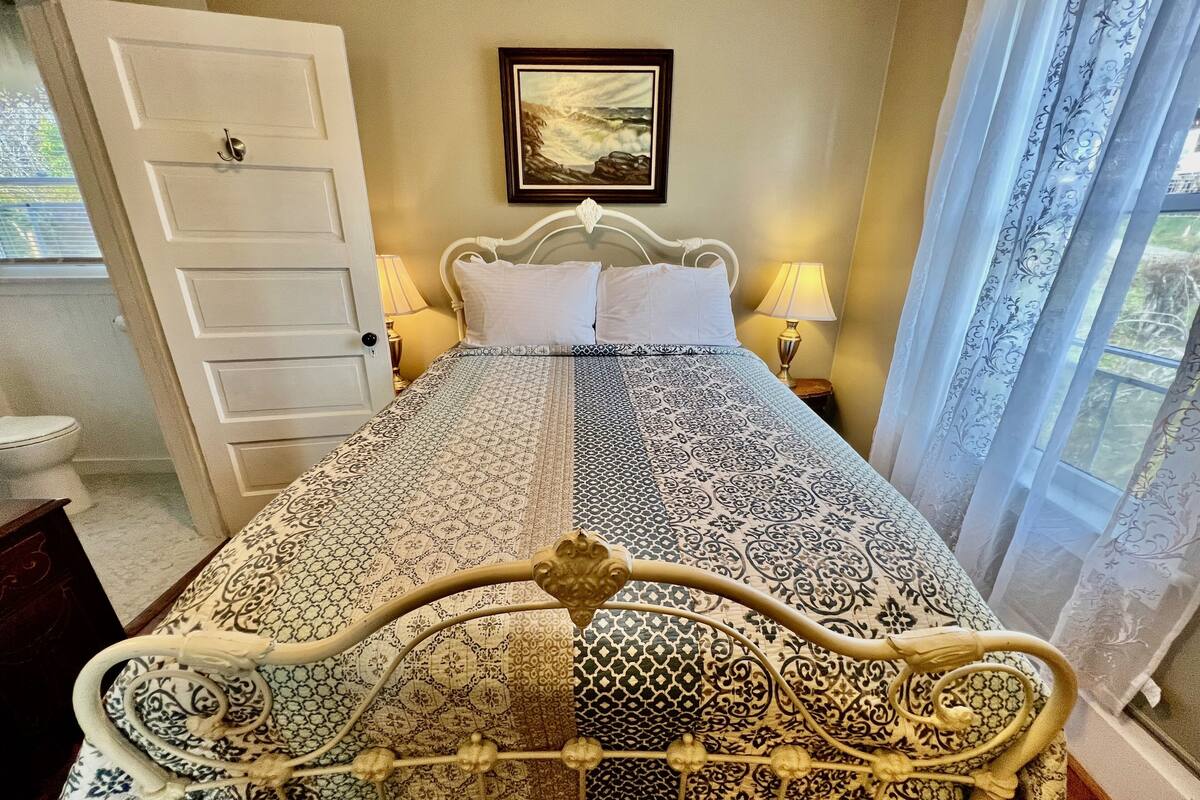 A neatly made bed with a patterned bedspread, two bedside lamps, and a framed picture on the wall.