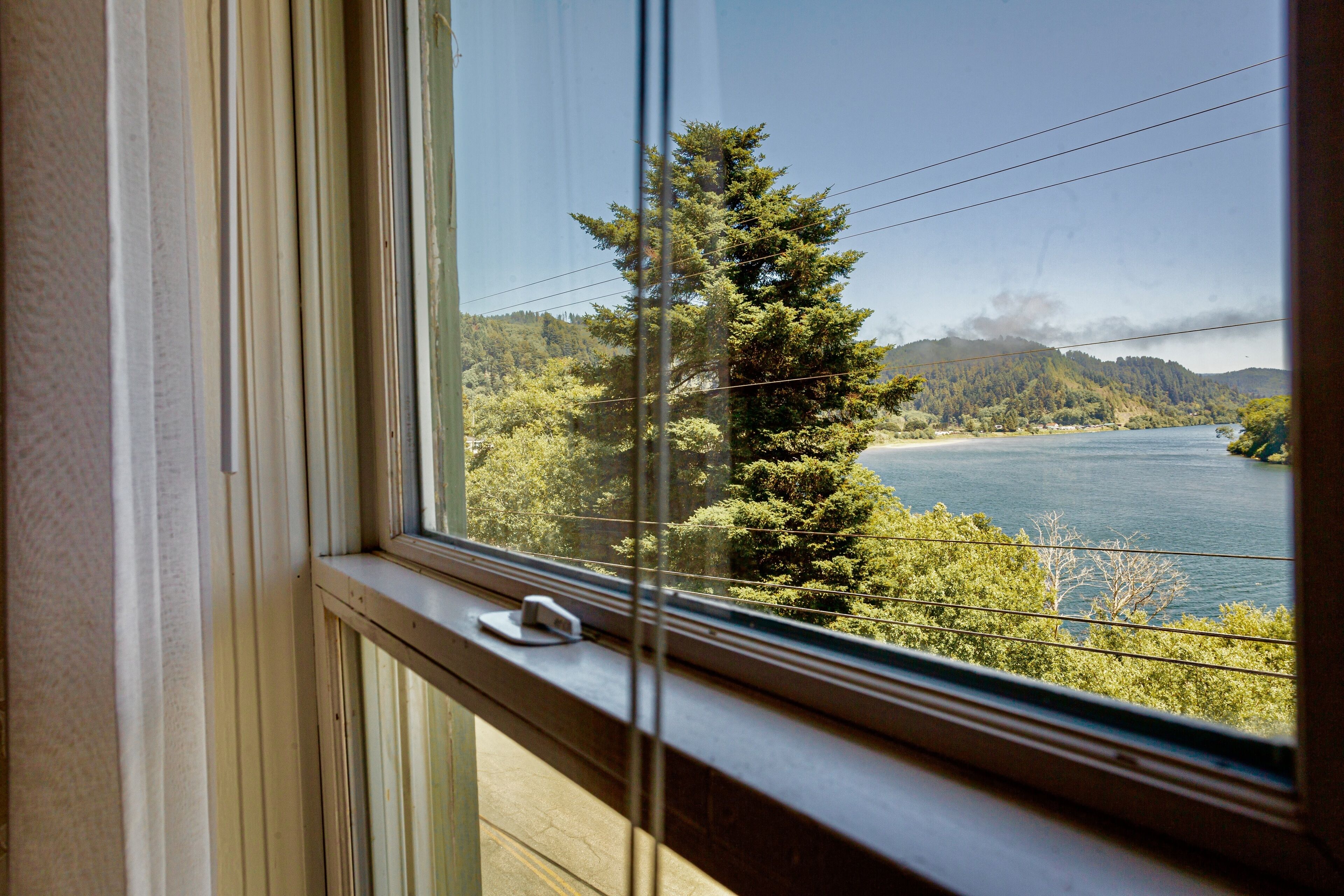 A window with a view of a lake, trees, and hills.
