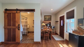 A kitchen with wooden flooring, a dining area with a table and chairs, a refrigerator, and a window with blinds. - The Historic Requa Inn  (Klamath)