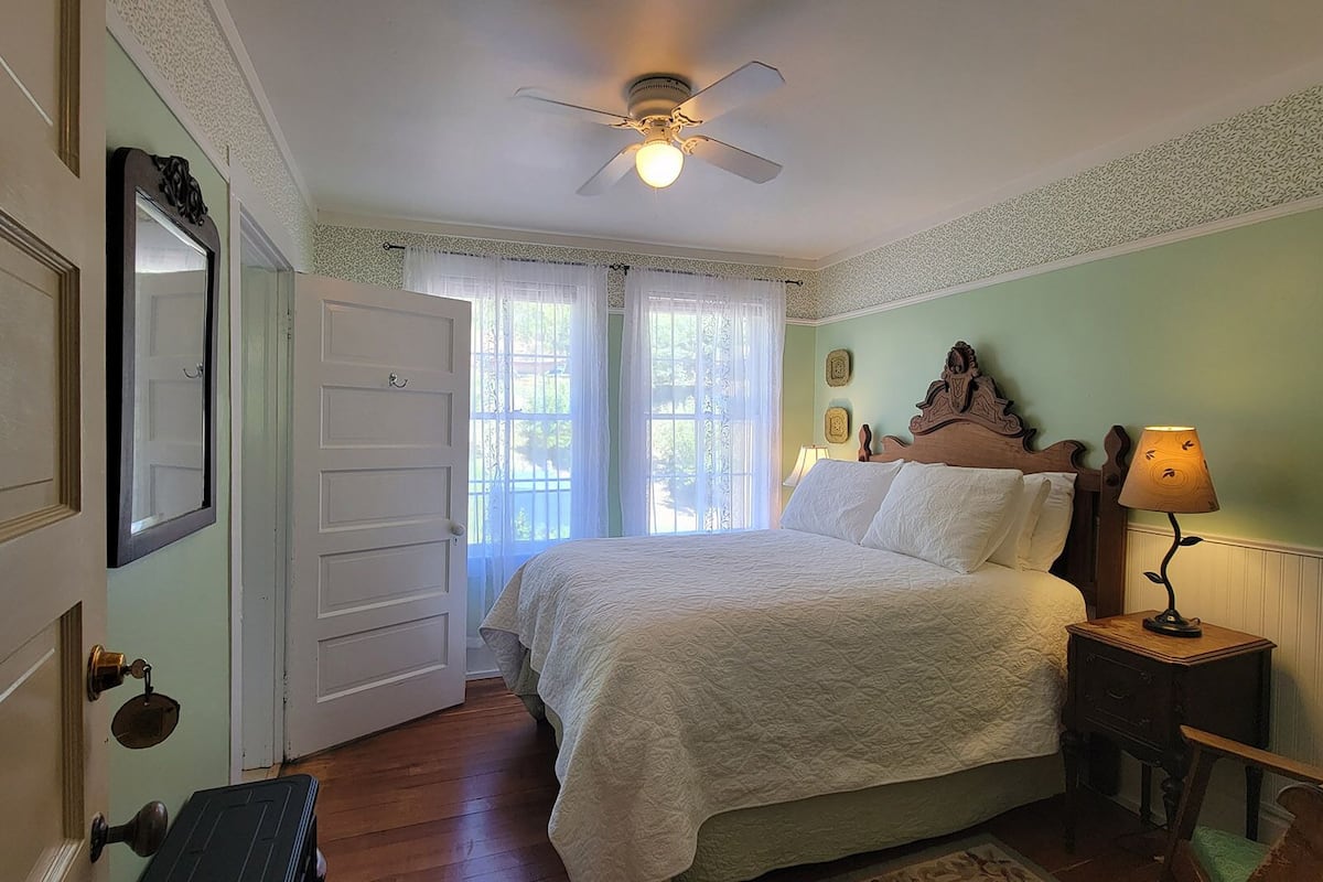 A bedroom with a bed, a nightstand, a lamp, a ceiling fan, and a door.