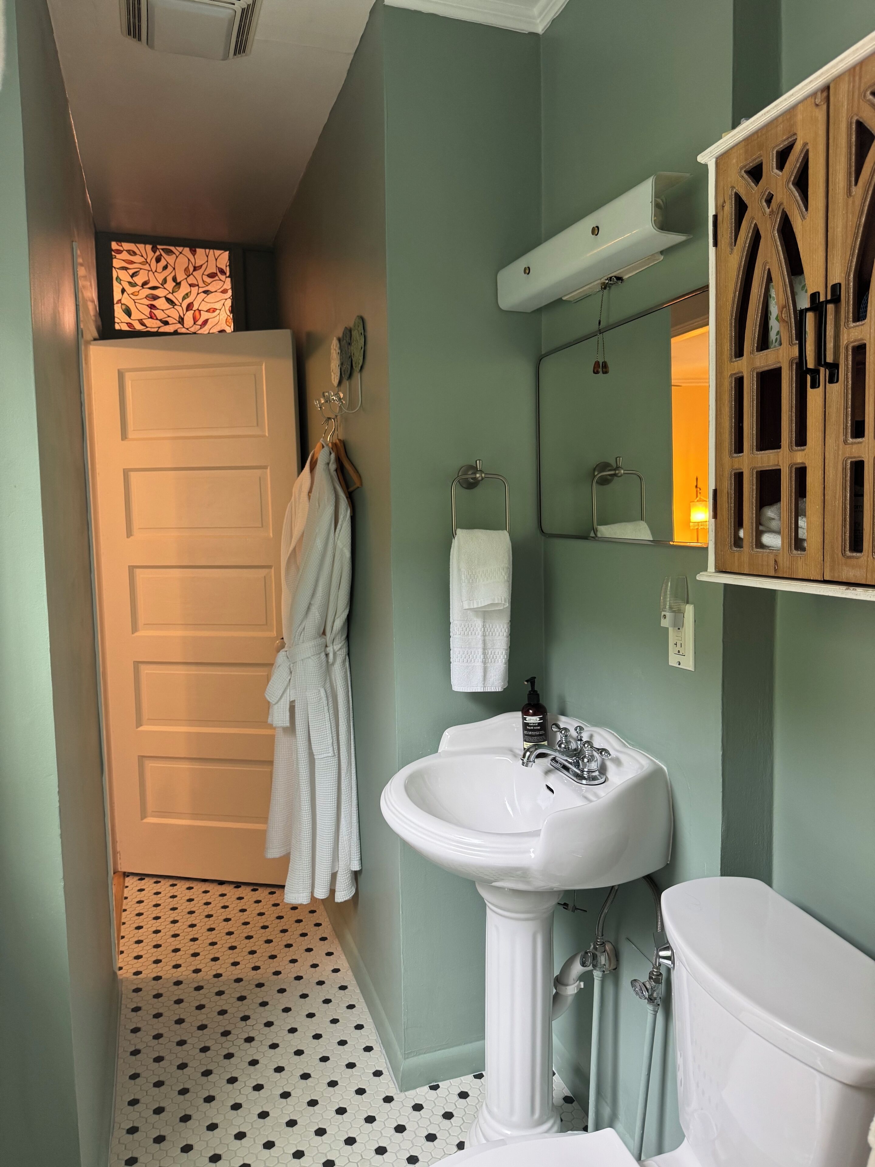 A bathroom with a white sink, a toilet, and a mirror. There is a wooden cabinet with a mirror above the sink.