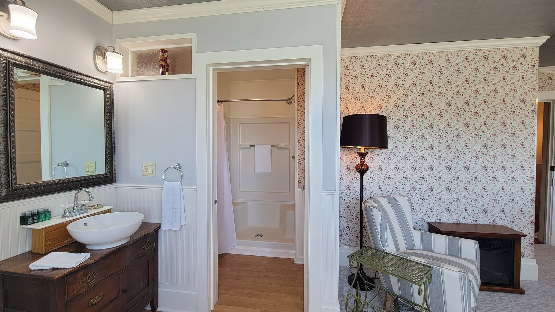 A bathroom with a large mirror, white sink, wooden vanity, and a shower area.