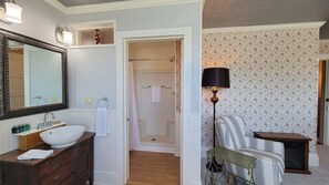 A bathroom with a large mirror, white sink, wooden vanity, and a shower area.