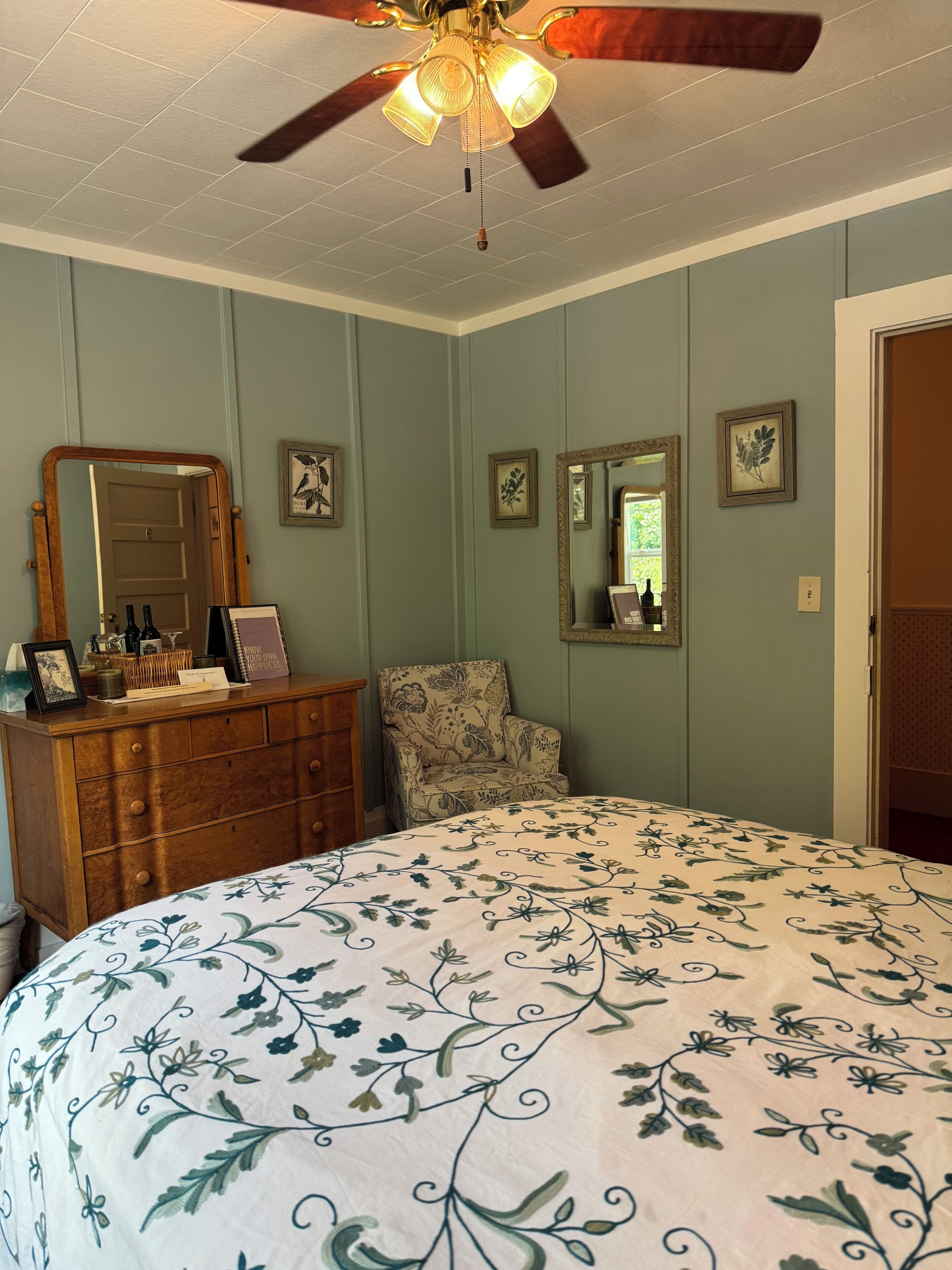 Een slaapkamer met een bed, een dressoir, een stoel en een plafondventilator.
