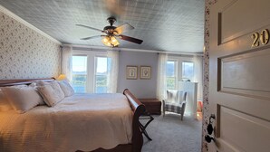 A bedroom with a bed, a ceiling fan, a bench, a chair, and a door with a number. - The Historic Requa Inn  (Klamath)