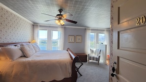 A bedroom with a bed, a ceiling fan, a bench, a chair, and a door with a number. - The Historic Requa Inn  (Klamath)