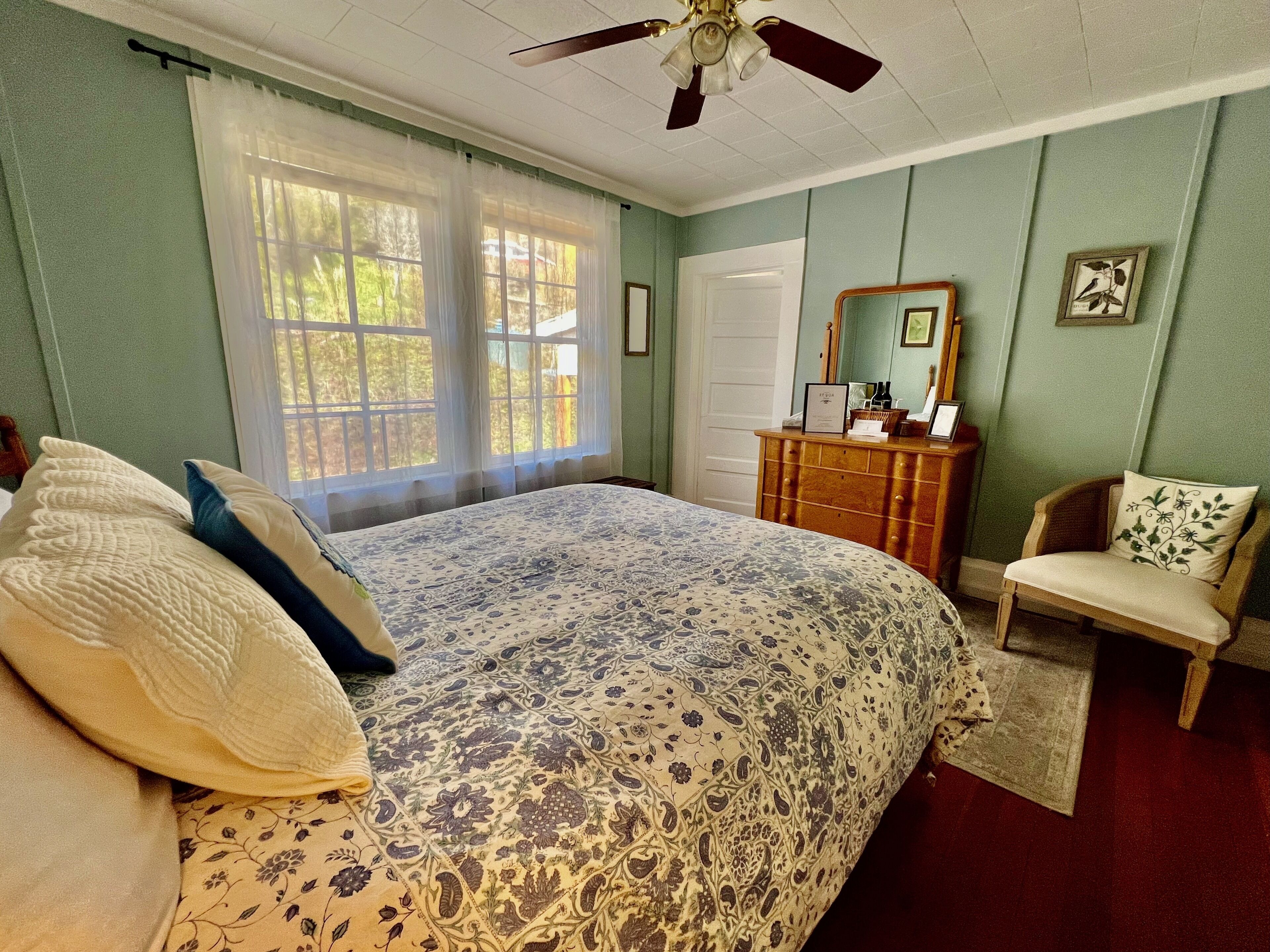 A bedroom with a large bed, a wooden dresser, a chair, and a ceiling fan.