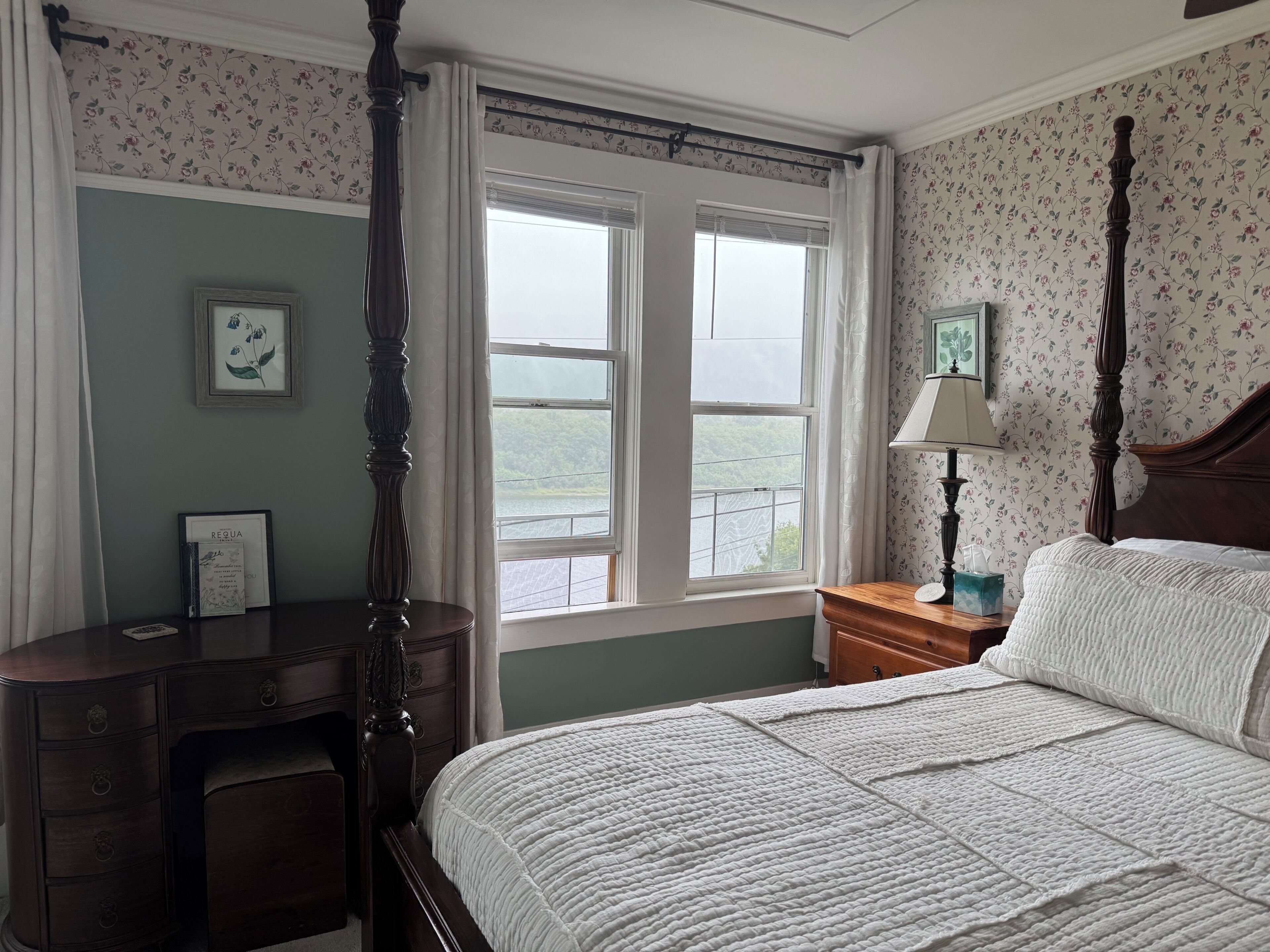 Une chambre à coucher avec un lit à baldaquin, un bureau et une fenêtre donnant sur un paysage verdoyant.