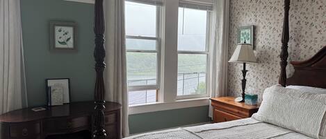Une chambre à coucher avec un lit à baldaquin, un bureau et une fenêtre donnant sur un paysage verdoyant.