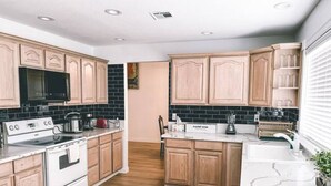 Een moderne keuken met houten kastjes, een zwart betegelde achterwand, een wit aanrechtblad en een inbouwoven.