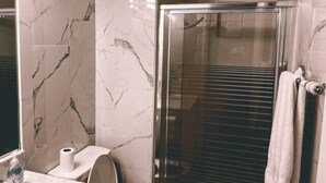 Een badkamer met een douchecabine van glas, marmeren wanden en een toilet.