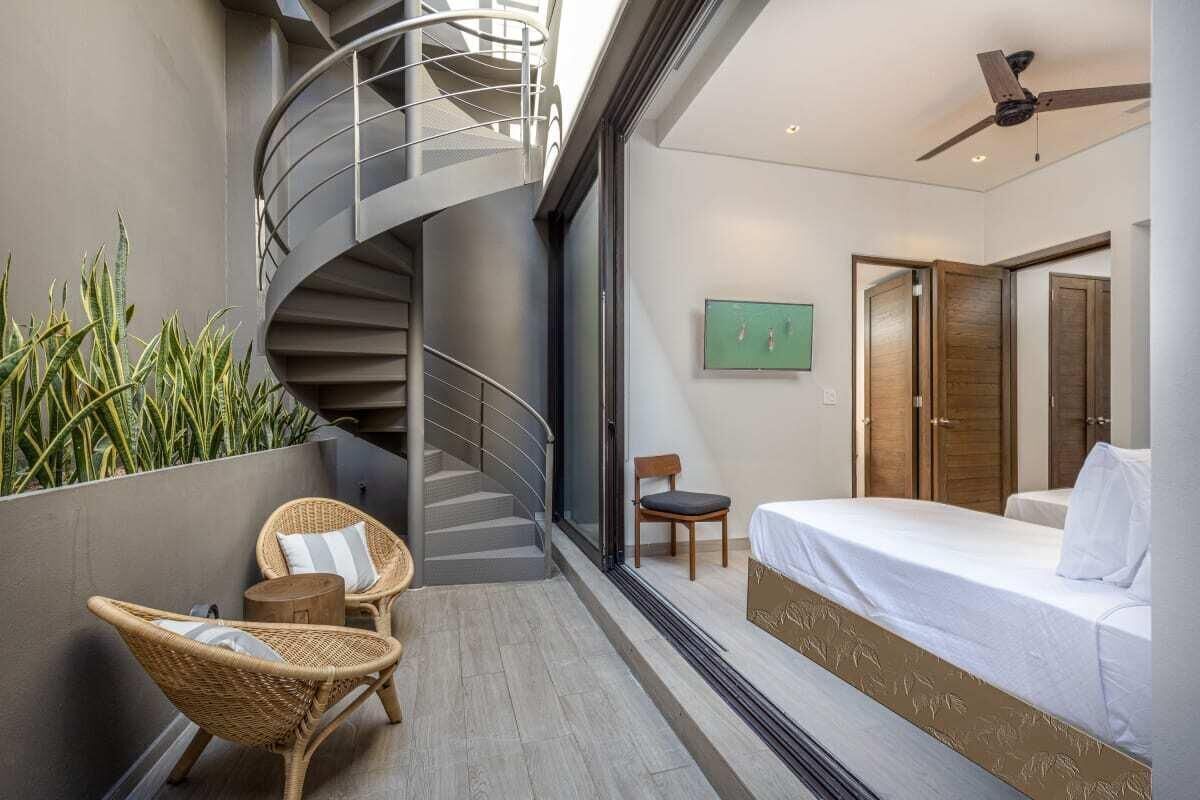 A modern bedroom with a bed, a chair, a small table, a spiral staircase, and a green wall with plants.
