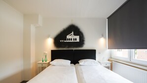 A hotel room with a large bed, two bedside tables, a wall-mounted artwork, and a window with a view. - Stay With Garden, Limburg (Kerkrade)