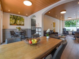 Un comedor amplio con una mesa de madera, sillas y un frutero. Se observa un sofá y una mesita de centro al fondo.