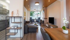 A modern living room with a sofa, chairs, a TV, and a wooden dining table. - Stay With Garden, Limburg (Kerkrade)