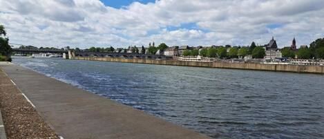 A riverside walkway with a stone path and a bridge in the background.