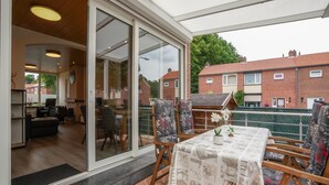 A patio area with a table and chairs, a view of the adjacent kitchen and living room, and a brick house in the background. - Stay With Garden, Limburg (Kerkrade)
