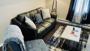 A living room with a dark leather sofa, a grey armchair, a small white coffee table, and a floor lamp.