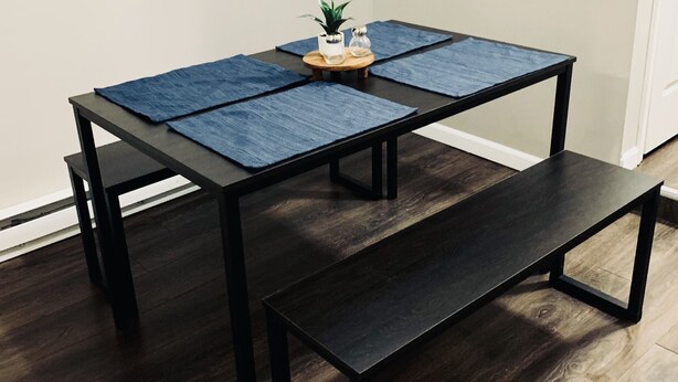 A dining table with a bench, a small plant, and salt and pepper shakers on a wooden table with blue placemats.