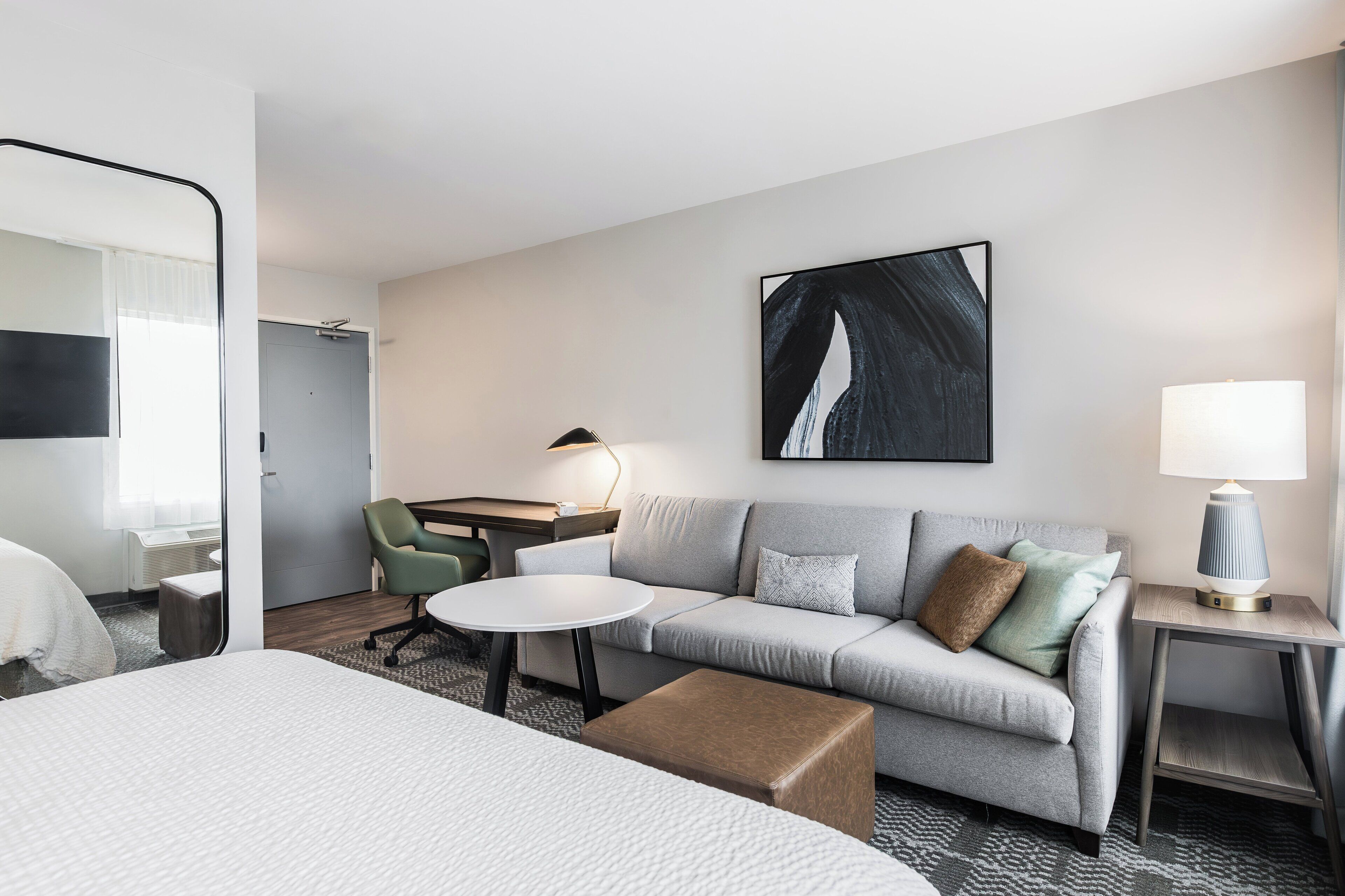 Une chambre d’hôtel moderne équipée d’un lit, d’un canapé, d’une petite table, d’un bureau et d’une lampe.