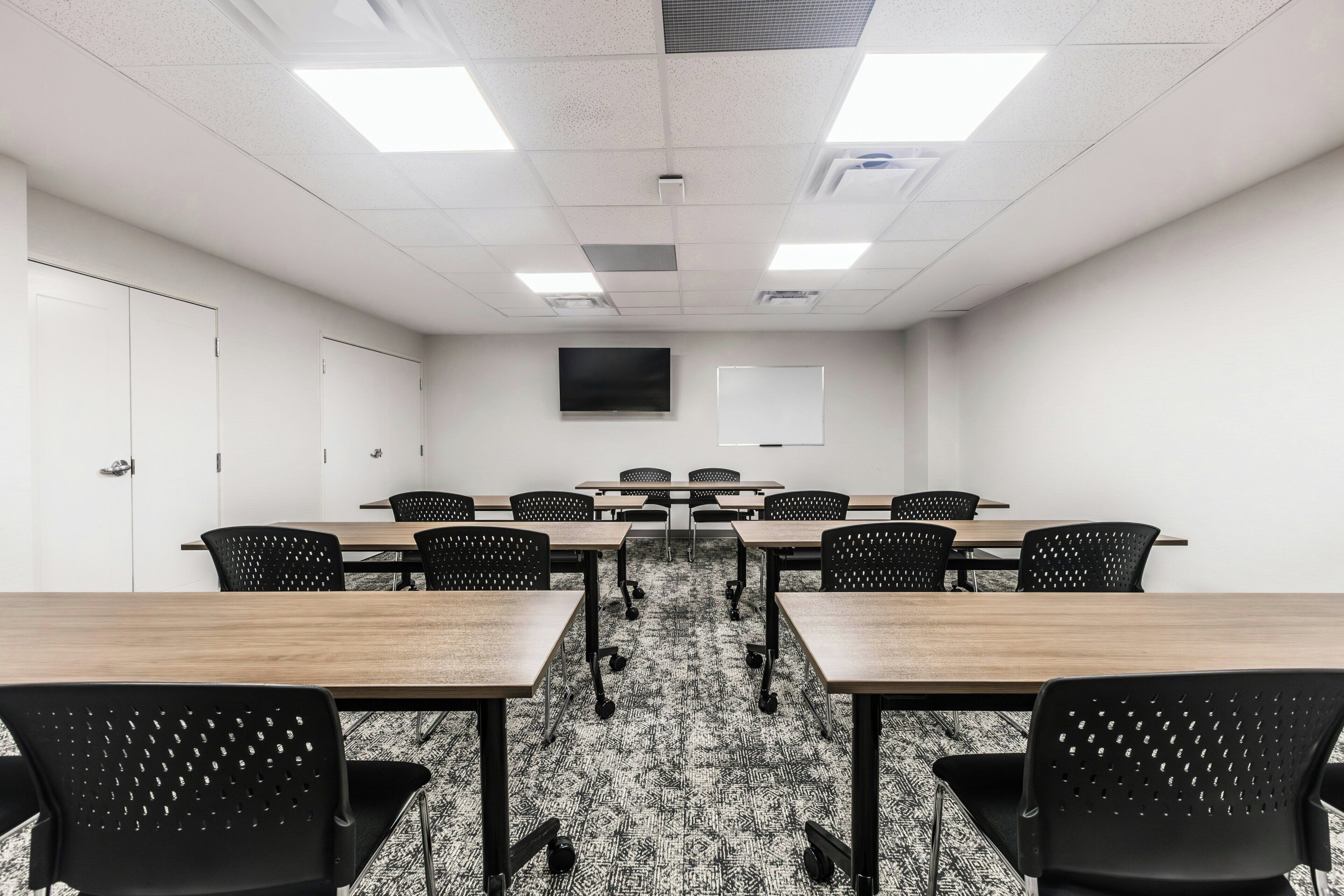 A conference room with a long table, multiple chairs, a whiteboard, and a flat-screen TV.
