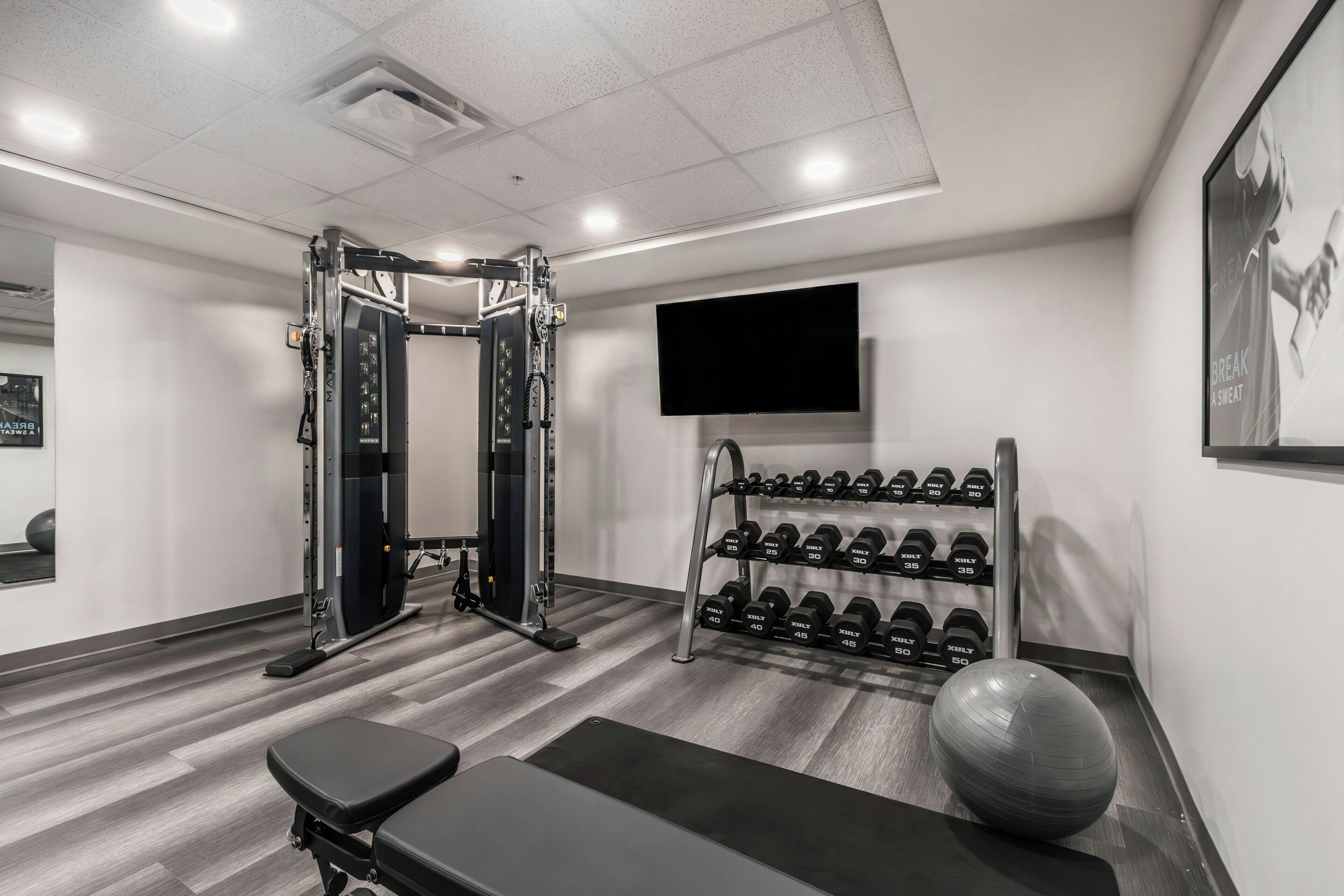 Une salle de sport équipée d’un support à squats, d’haltères, d’un banc et d’un vélo d’appartement.