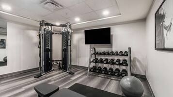 Une salle de sport équipée d’un support à squats, d’haltères, d’un banc et d’un vélo d’appartement.