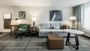 Een hotelkamer met een bank, een bureau, een stoel, een lamp, een tafel en een vloerkleed.