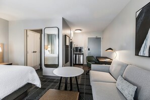 Een hotelkamer met een bed, een zithoek met een bank en fauteuil, een kleine tafel, een spiegel en een kitchenette.