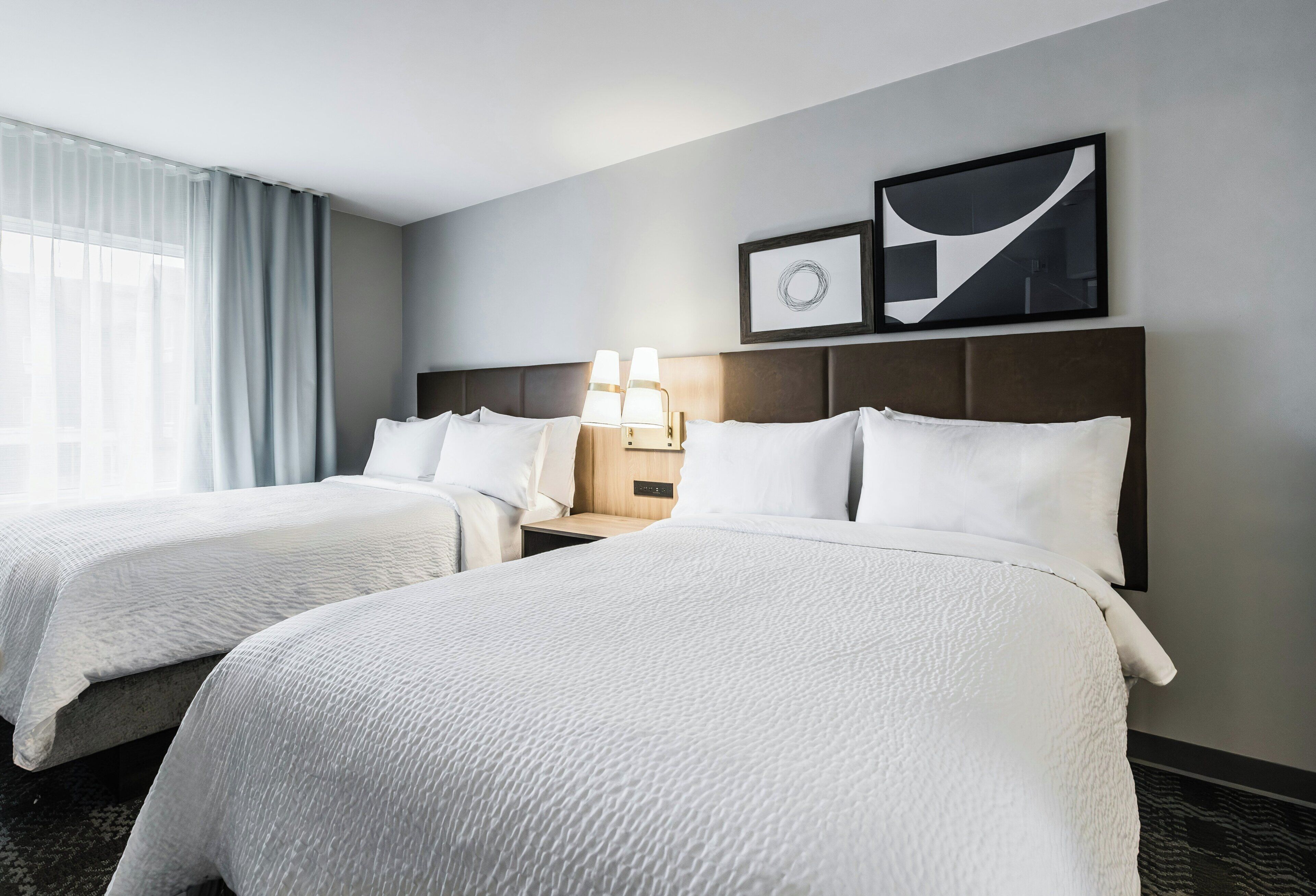 Habitación de hotel con dos camas, una mesita de noche con lámparas y una obra de arte en la pared.