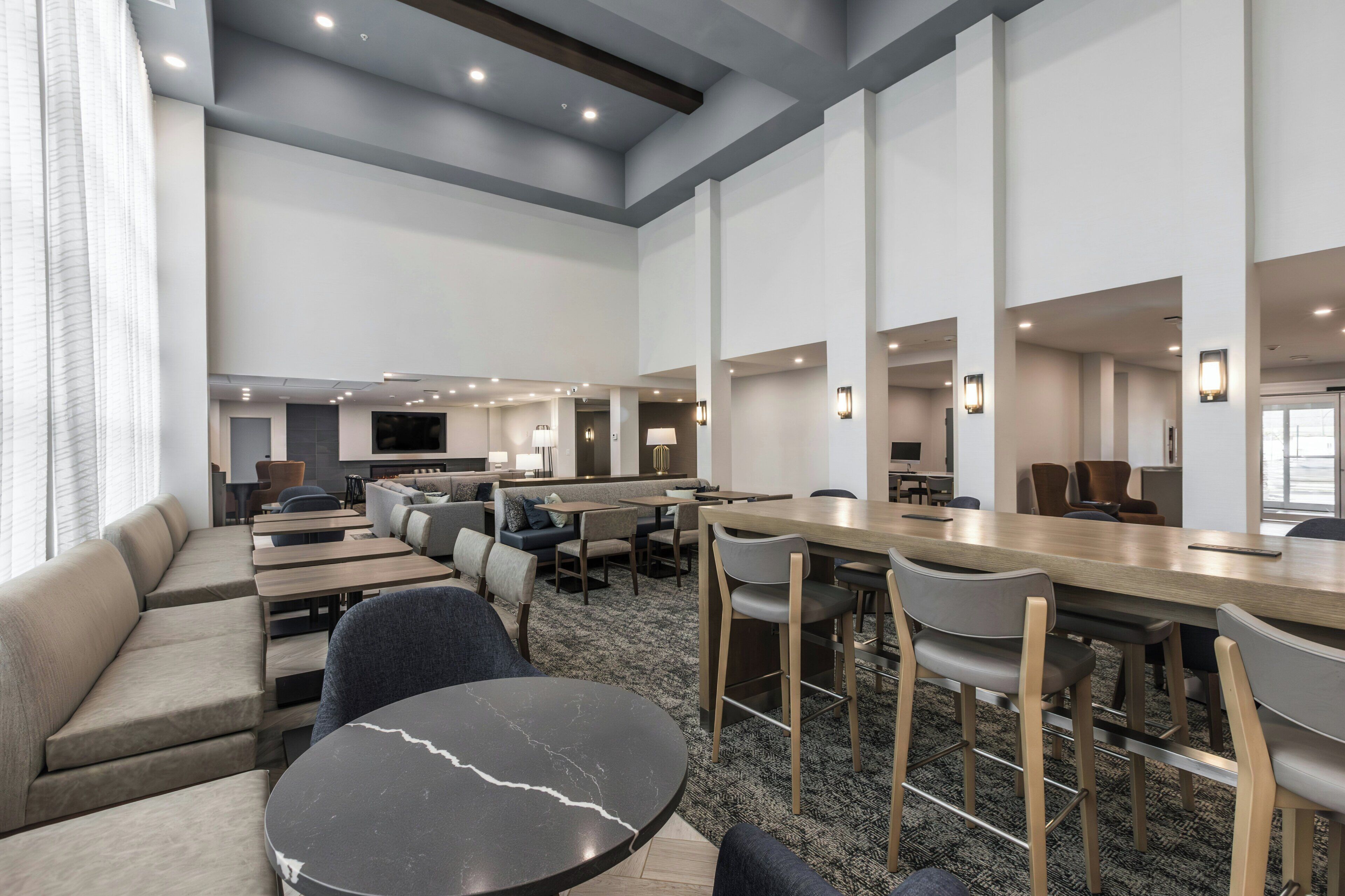 A modern hotel lobby with seating areas, a bar, and a television.
