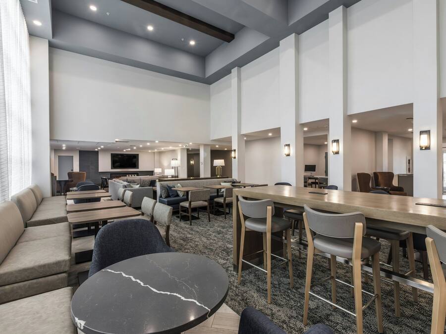 A modern hotel lobby with seating areas, a bar, and a television.
