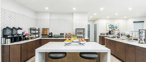 Una cocina moderna con una isla central, taburetes de bar y diversos electrodomésticos.