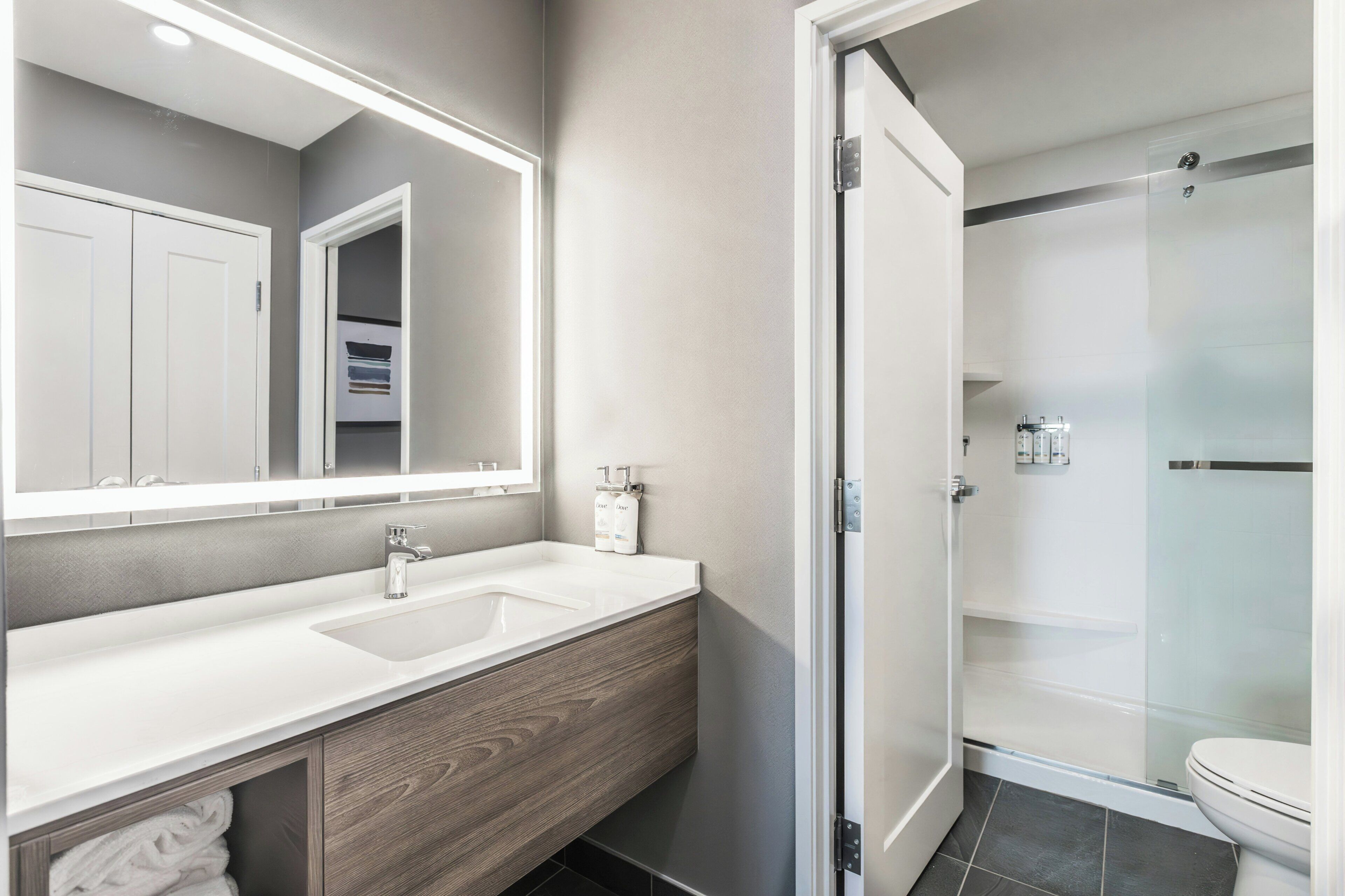 A modern bathroom with a double sink vanity, a large mirror, and a glass-enclosed shower.