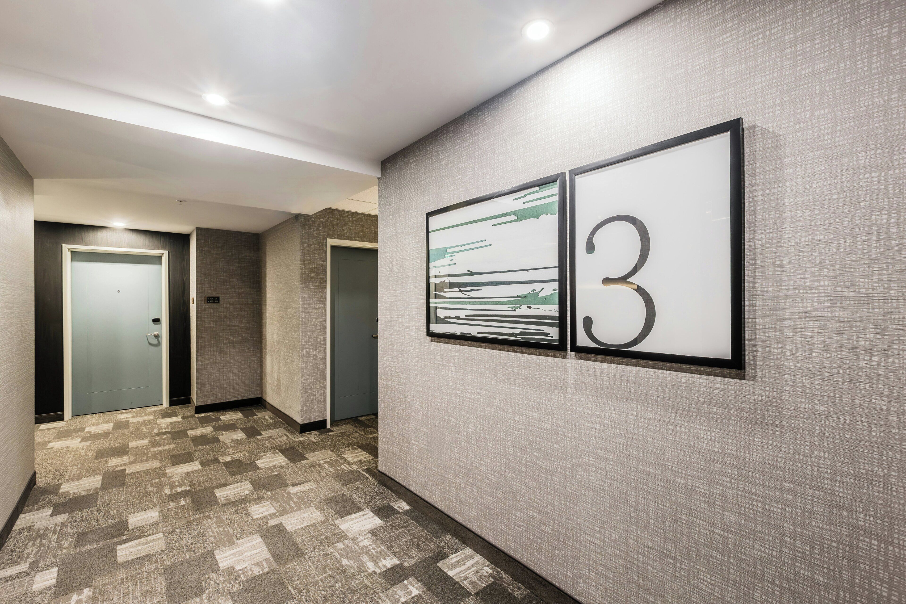 A hallway with a patterned carpet, a door, and a wall-mounted number sign indicating room 3.