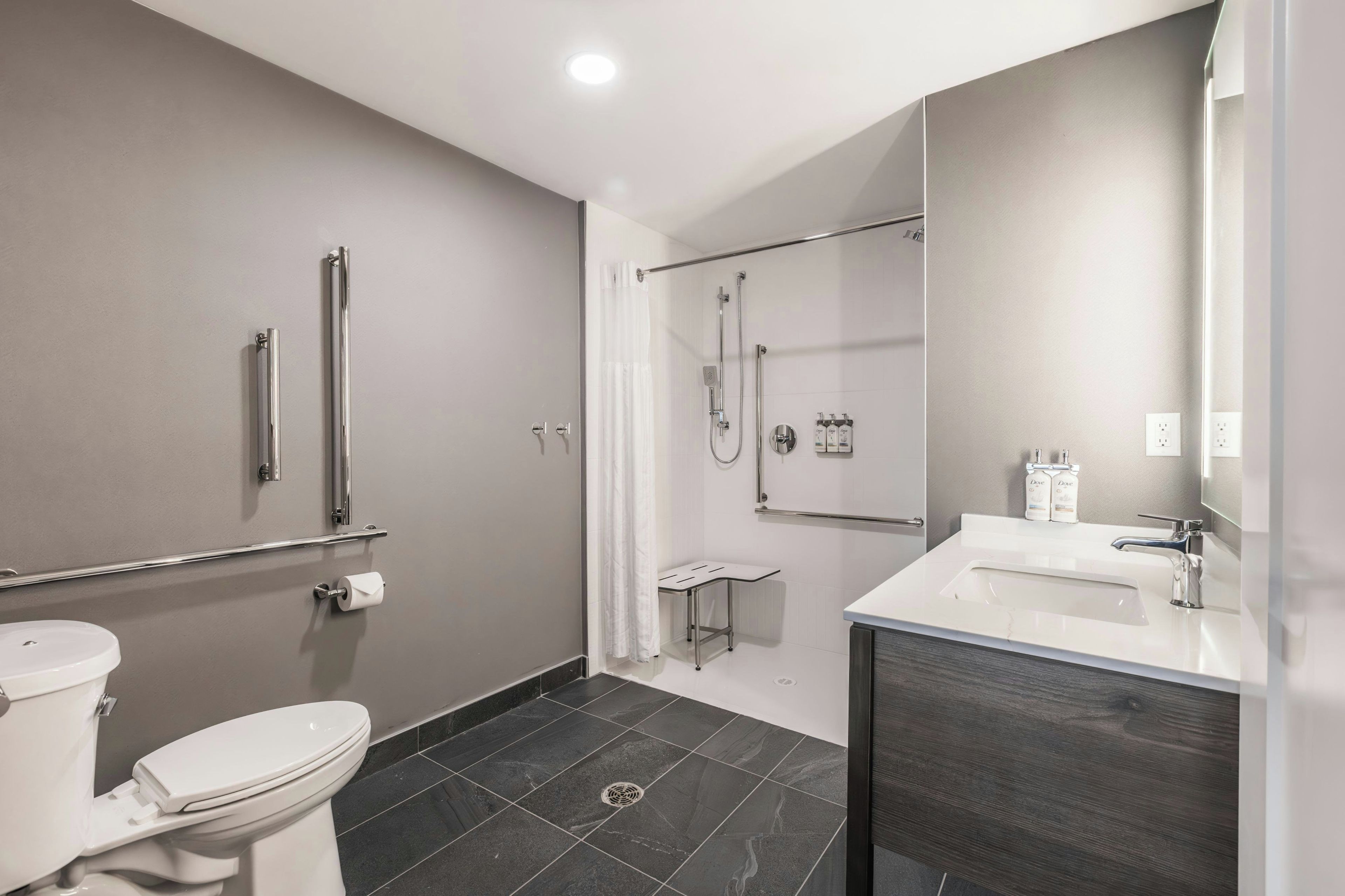 A modern bathroom with a toilet, a shower with a glass door, a vanity with a mirror, and a toilet paper holder.