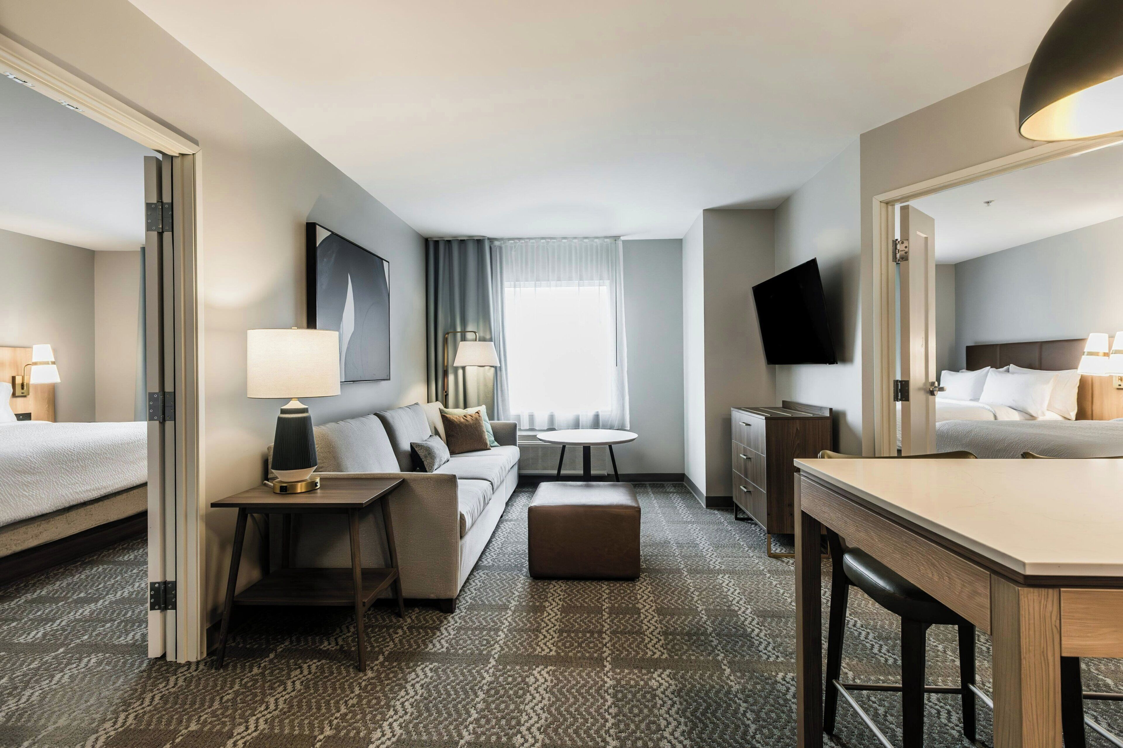 A hotel room with a bed, a sofa, a desk, a chair, a TV, and a window with curtains.