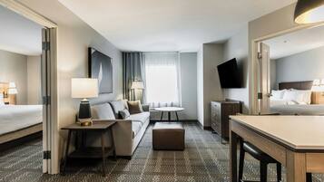 A hotel room with a bed, a sofa, a desk, a chair, a TV, and a window with curtains.