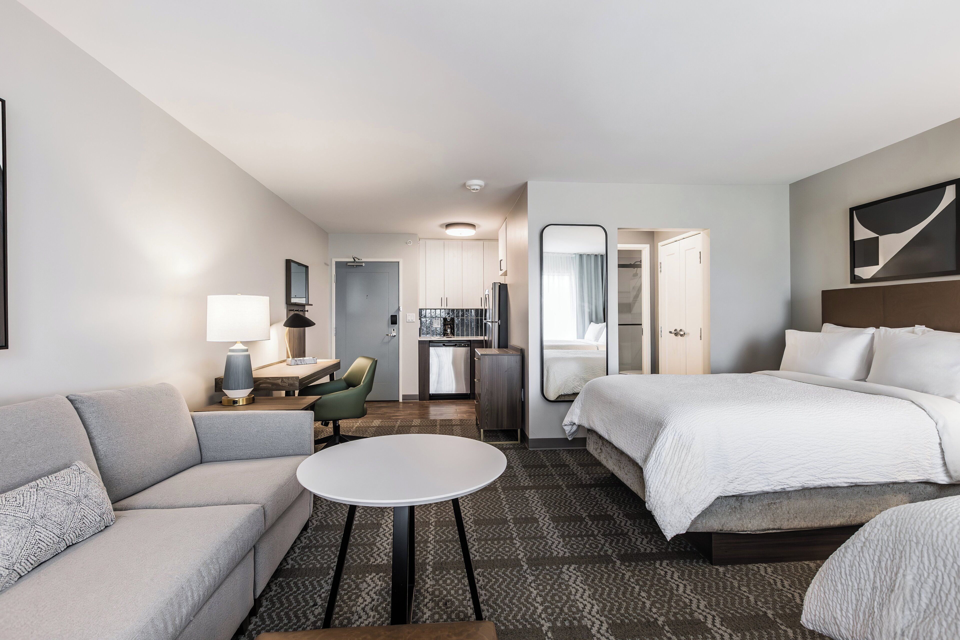 Une chambre d’hôtel comprenant un lit, un canapé, une petite table, un bureau, une chaise, un miroir et une kitchenette.