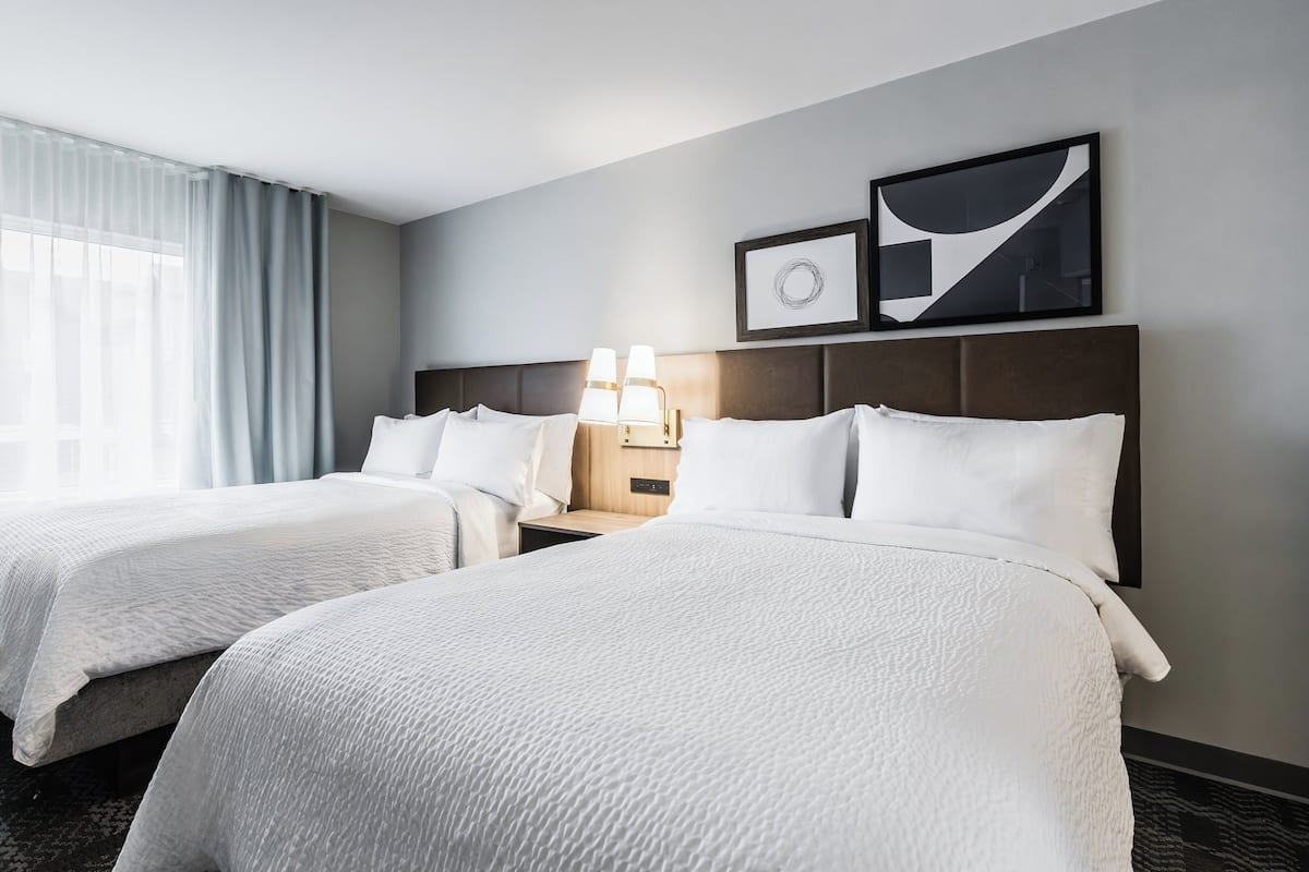 Ein Hotelzimmer mit zwei Betten, einem Nachttisch mit Lampe sowie zwei gerahmten Bildern an der Wand.
